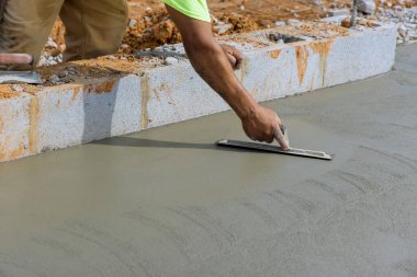 Duvarcılık işçisi çelik bir malayı tutar. Çelik bir malayla beton zeminde alçı betonu düzleştirir.