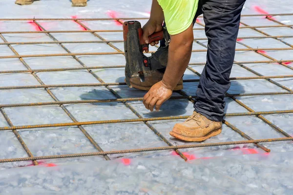 Construction worker twist steel bars with wire rod reinforcement into cement foundations using tool known as the rebar tying tool