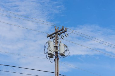 Elektrik kablosu, mavi gökyüzü arka planına sahip elektrik kablolarıyla çevrili ahşap bir sütunda görülür.