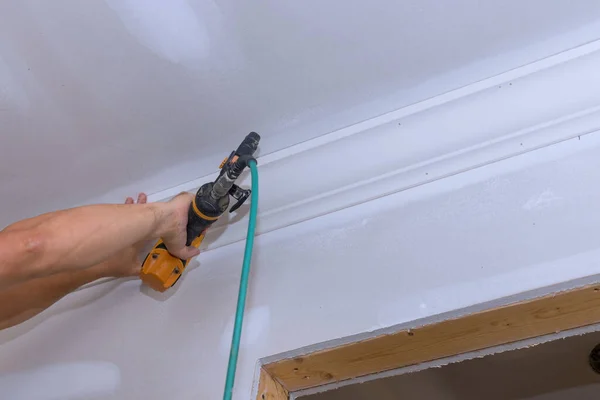 Ceiling corner crown molding installation with the use of an air nail gun by a carpenter to new home