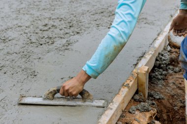 Mason worker is holding steel trowel and smoothing plastering new sidewalk on wet freshly poured concrete in construction site