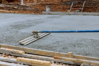 A construction worker is working on a new sidewalk that has just been poured on wet concrete while holding steel fresno concrete trowel