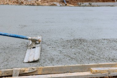 Worker is holding a steel fresno concrete trowel and smoothing plastering over freshly poured concrete that is wet in construction zone