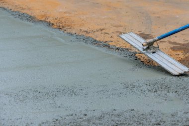 Mason worker is holding steel fresno concrete trowel and smoothing plastering new sidewalk on wet freshly poured concrete in construction site