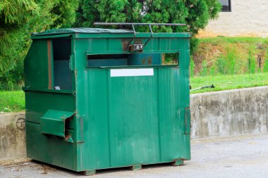 There is a container near an apartment building where bin garbage is collected