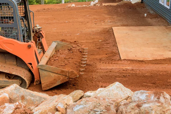 Small tractor working with earth moving to land leveling in construction site near new house