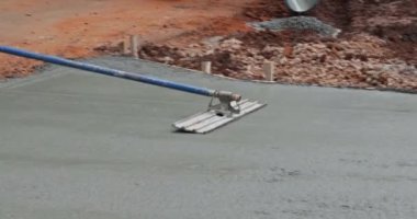 Worker is holding a steel fresno concrete trowel and smoothing plastering over freshly poured concrete that is wet in construction zone