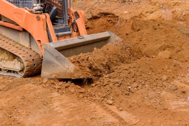 There is a small tractor working with the earth moving equipment for leveling land near new house.
