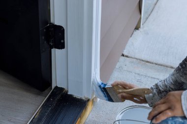 Using paintbrush a wooden molding carpenter works on painting wooden moldings for doors