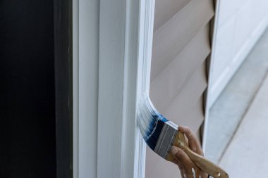 Contractor painter uses a paintbrush as he works on painting the wooden moldings door trim