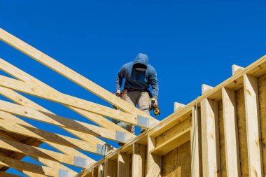 A worker hammering wooden frame beams into rafters roof using an air hammer in household construction project
