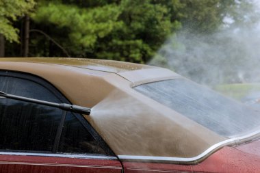 Worker is washing his car under high-pressure jet spraying water on it as well as cleaning it
