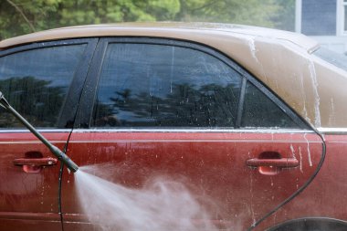 Worker washes his car under high pressure jet sprays of water along with cleaning his car at the same time