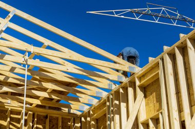As part of a household construction project, worker uses an air nail hammer to wooden frame beams the roof rafters