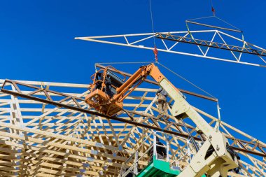 Construction worker using air hammer nailing beams of wooden frame roof rafters in his domestic building with wooden framework beams