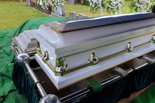 As part of the funeral service in a cemetery, coffin is placed on an automatic elevator and is lowered into grave before burial