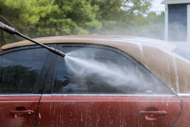 Worker washing his car under high pressure jet spraying water along with cleaning his car