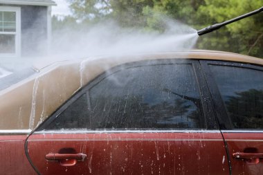 Adam arabasını yüksek basınçlı jetle yıkıyor.