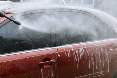 Arabasını yüksek basınçlı jetin altında yıkarken arabayı fırçayla temizliyor.