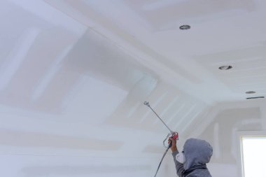İşçi astar boya duvarlı ve tavan boyalı sprey tabanca kullanıyor.