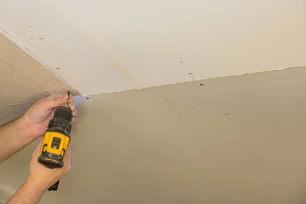 The worker uses a screwdriver to attach the drywall to the ceiling