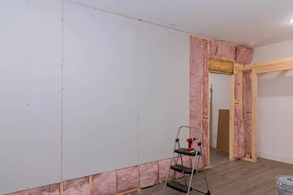 The drywall is screwed to beams framing of wall after sound and thermal insulation has been installed in new home.