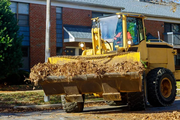 During autumn, workers from municipalities over the entire city clean up fallen leaves near houses by excavators trucks