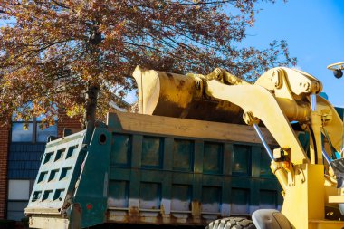Sonbahar mevsimi yaklaşırken, belediye çalışanları buldozer ve kamyonla evlerin yakınındaki düşen yaprakları kaldırıyor.