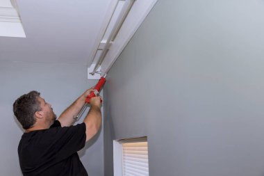 İnşaat işçisi şırıngası Cornice ve duvar arasındaki dikişleri akrilik lateks dolgu macunuyla dolduruyor.