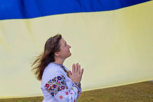 Young woman prays for Ukraine near Ukrainian flag as prays for Ukraine