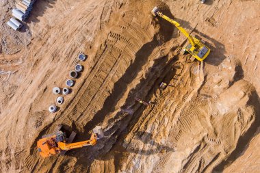 Kazıcılar yeraltı fırtına kanalizasyonları için boru döşemek için inşaat sahasına siper kazıyorlar.