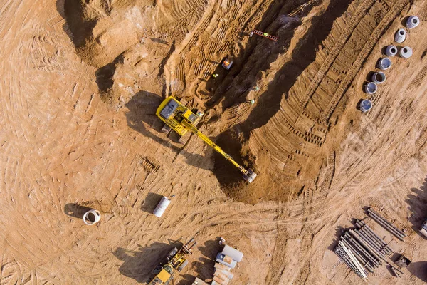 Excavator digs trench for laying of underground storm sewer pipes on construction site and connects them to an underground sewer line.