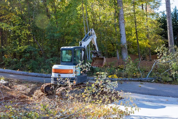 Fallen tree after storm damaged fence after hurricane an uprooted trees fell in street with tractor cleanup raise fallen trees