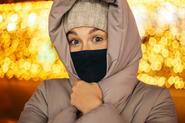 Aman Tanrım! Dışarıdaki korkmuş kadın şaşırdı. Maske takıyor. Gece şehir ışıkları, kış soğuğu çelenkleri. Noel ağacı Yeni Yıl atmosfer aydınlatma dekorasyonları boşluğu kopyalar