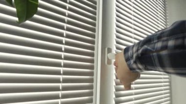 Erkek adam elini kapatır odasına temiz hava girmesi için pencereyi açar, güneş ışığı güneş evi dairelerine girer..
