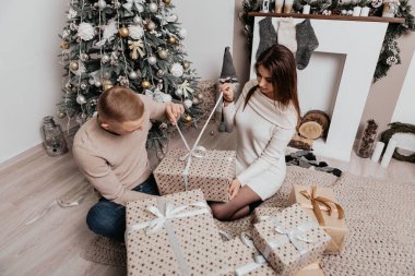 Güzel, genç, romantik bir çift hediyelerini açıyor. Çiçekler ev içinde rahat bir iç atmosfer. Yeni yıl ağacı süslemeleri. 