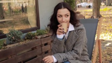 Güzel öğrenci girişimci kadın şezlongda oturuyor sokak kafesi restoranının önünde sıcak içkinin tadını çıkarıyor kahve içiyor el ele tutuşup şehir manzaralı park manzaralı arka planda geziniyor.