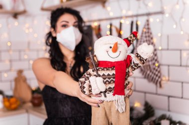 Mutfaktaki üzgün kadın oyuncak havuç burunlu yumuşak oyuncak kardan adam burunlu, mavi maske takan yeni yıl akşamı, Noel süslemeli ev. Tatil fotokopi yeriyle tebrik ederim. 