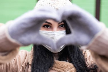 Güzel bir kadın sıcak palto giyip kutlama yapıyor. El ve kalp şeklinde aşk işareti yapıyor. Soğuk hava, kış tatilleri fuarı, tatil beldesi. Yeni yıl Noel süslemeleri