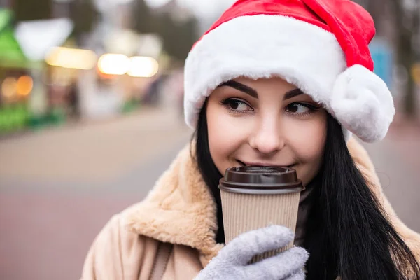 若いかなり女性は熱い飲料コーヒーか紅茶エコフレンドリーなカップを保持することを祝うミトン 寒い天候 冬の市場の休日の公正 旅行リゾート 新年の帽子クリスマスツリーの装飾 — ストック写真