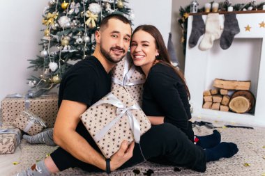 Güzel, genç, romantik bir çift hediyelerini açıyor. Çiçekler ev içinde rahat bir iç atmosfer. Yeni yıl ağacı süslemeleri. 