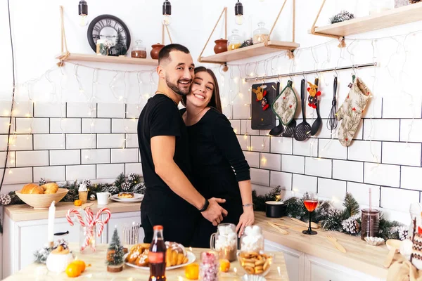 可爱的笑着的年轻夫妇站在厨房亲吻拥抱家舒适的室内空气新年装饰节日派对庆祝概念冬夜复制空间 — 图库照片