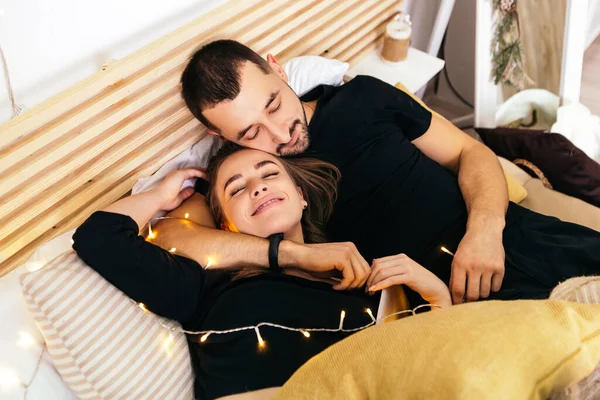 Υπέροχο Νεαρό Ρομαντικό Ζευγάρι Ξαπλωμένο Κρεβάτι Φιλιά Αγκαλιά Γιρλάντες Σπίτι — Φωτογραφία Αρχείου