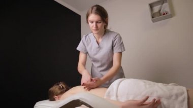 Kadın masör terapist sağlıklı sırt masajı yapıyor profesyonel terapi ellerini yağlıyor. Kanepe masasında uzanan kız güzellik salonunda vücut bakımı konseptinde masaj yaptırıyor, yavaş çekimde tedavi oluyor.