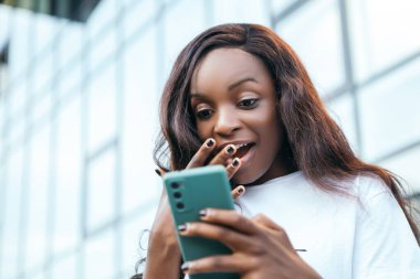 Gülümseyen bir afro-amerikan güzel kadını şaşırttı. Elinde telefon, internette sohbet ediyor. Arkadaşlarıyla sohbet ediyor.
