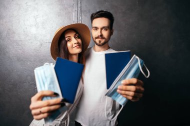 Gülümseyen çiftin kucaklaşması. Pasaportlar ve tek kullanımlık mavi maskeler. Karantina süresince sıcak iklimlerde tatil yapmaya hazır koca eşi. 