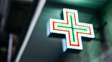 Odaklanamayan bokeh neon neon parlak yeşil parlayan kırmızı ışıklı şehir eczanesi çapraz işaretli ampuller Coronavirus pandemik karantinası sırasında şehrin binasında gece vakti