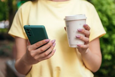 1 Ekim, Uluslararası Kahve Günü! Yeşil ağaçların dışındaki park kapalı, el telefonu, plastik beyaz bardak sıcak içecek kahve molası yaz tatilleri, fotokopi alanı.