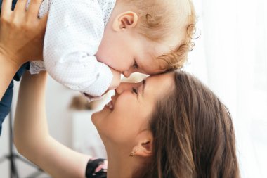 Küçük tatlı çocuk, kızıl saçlı bebek annesiyle oynaşıyor, oğlunu öpüyor. Yeni yürümeye başlayan çocuk evde tulum ve beyaz gömlek giyerek eğleniyor. Mutlu çocukluk, aile aşkı kavramı