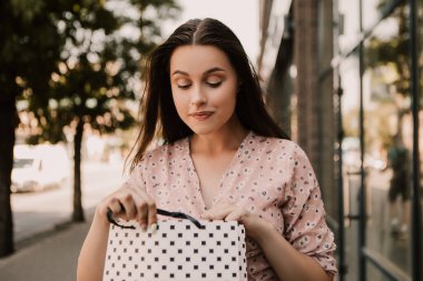 Surprised lady open and look into bags shopper woman dressed pink flower pattern dress carrying enjoying new clothes packs things after shopping buyings sales black friday concept